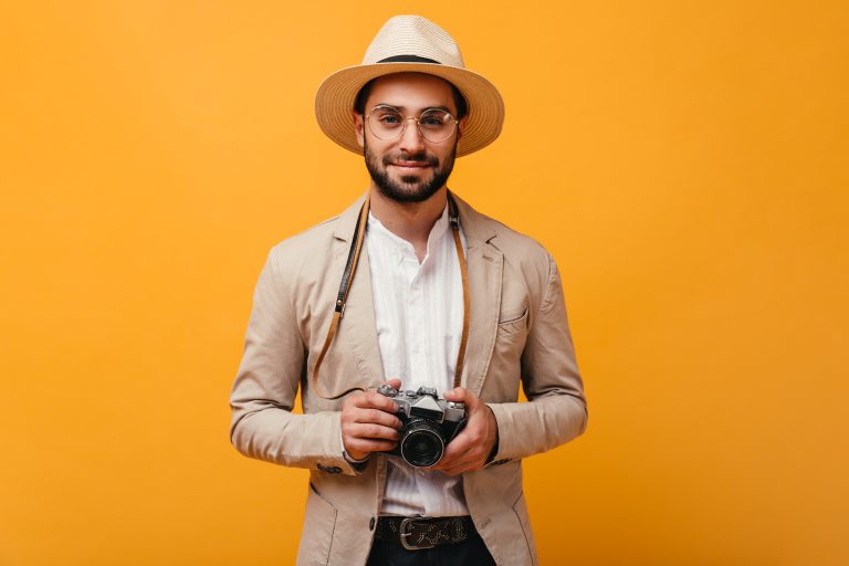 Smiling man in beige outfit holding retro camera on orange background
